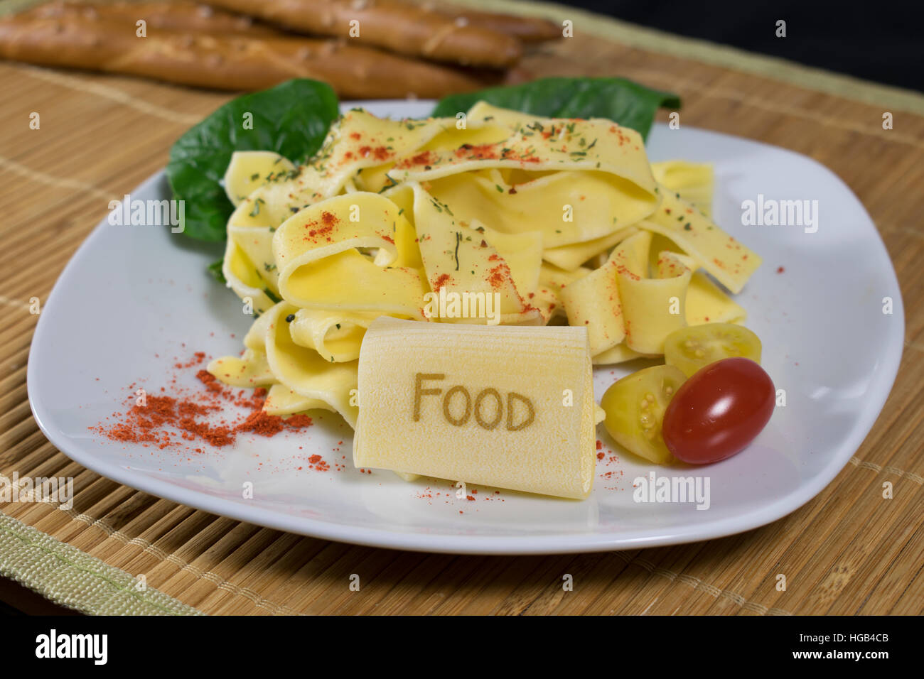 Nudelgericht gekleidet auf einem weißen Teller mit Blattspinat und Tomaten dekoriert. Auf der vorderen Noodle ist das Wort Essen. Stockfoto
