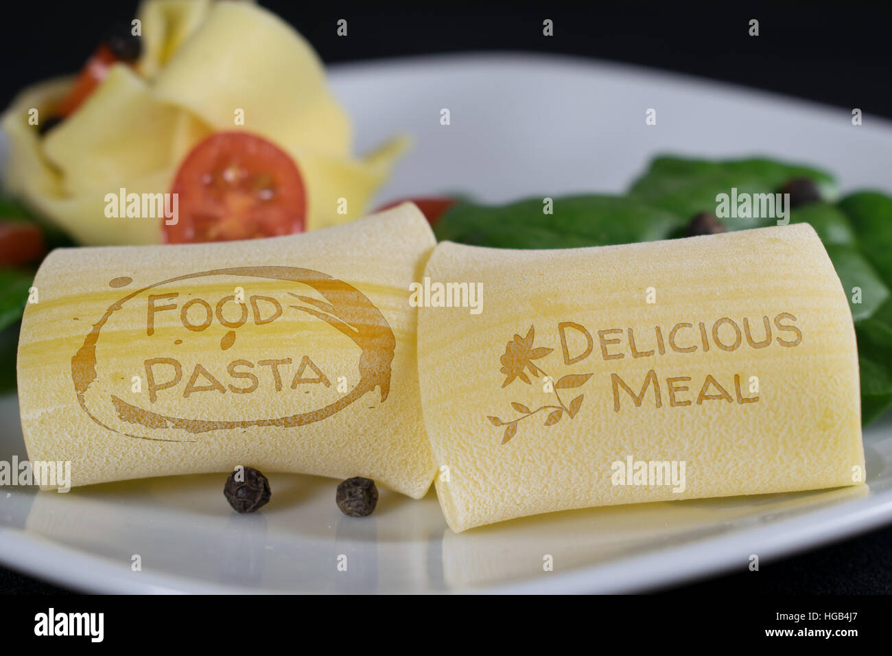 Auf einem weißen Teller sind 2 Nudeln mit dem Schriftzug "Essen Pasta - lecker Essen" im Vordergrund. Im Hintergrund sind weitere Nudeln garniert Witz Stockfoto