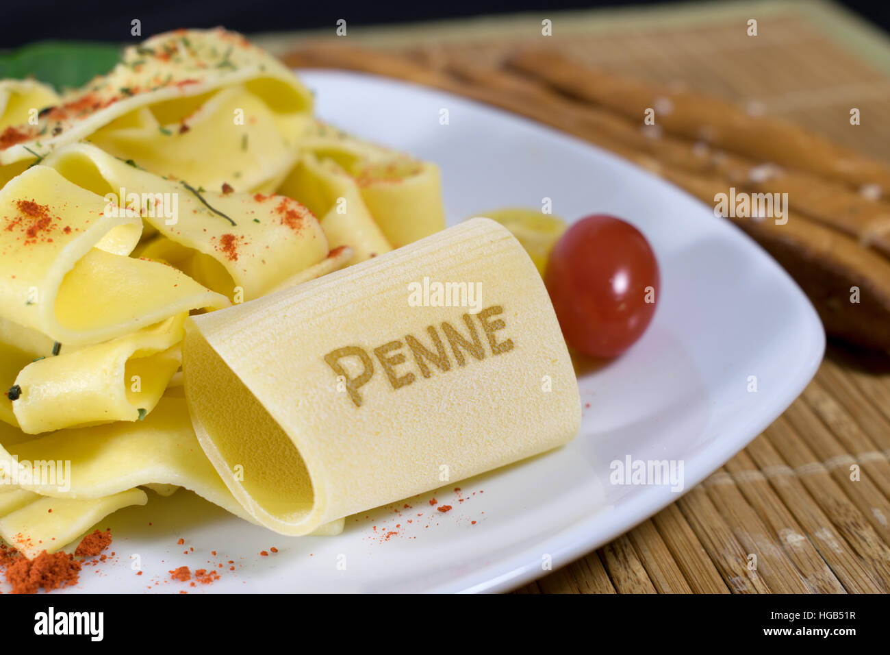 Nudelgericht gekleidet auf einem weißen Teller mit Blattspinat und Tomaten dekoriert. Auf der vorderen Noodle ist das Wort Penne. Stockfoto