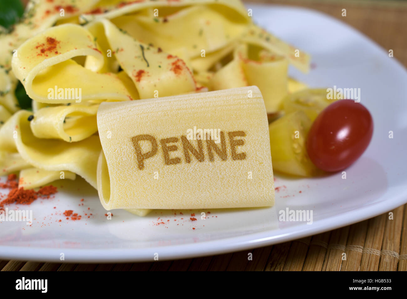 Nudelgericht gekleidet auf einem weißen Teller mit Blattspinat und Tomaten dekoriert. Auf der vorderen Noodle ist das Wort Penne. Stockfoto