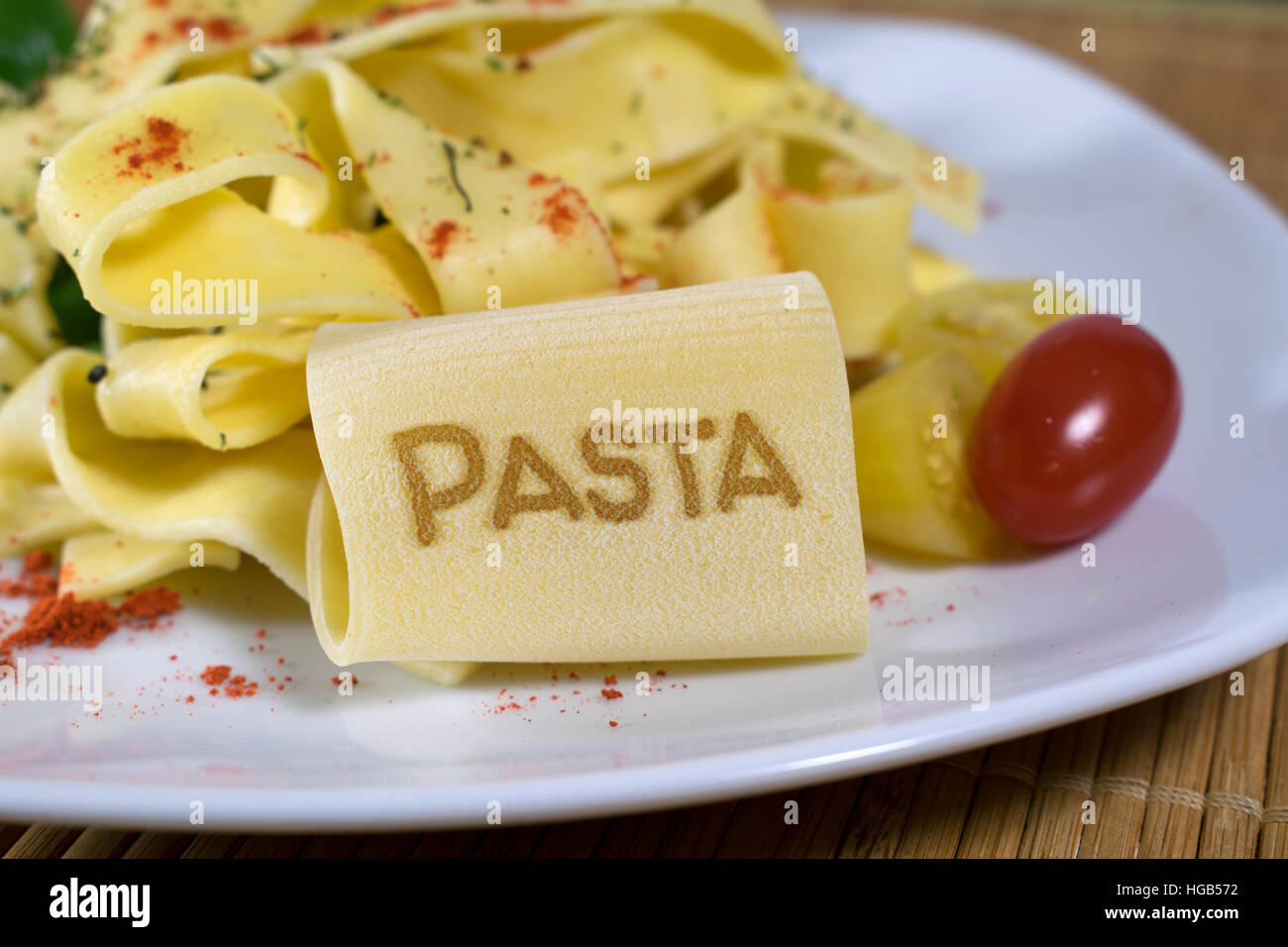 Nudelgericht gekleidet auf einem weißen Teller mit Blattspinat und Tomaten dekoriert. Auf der vorderen Noodle ist das Wort Pasta. Stockfoto