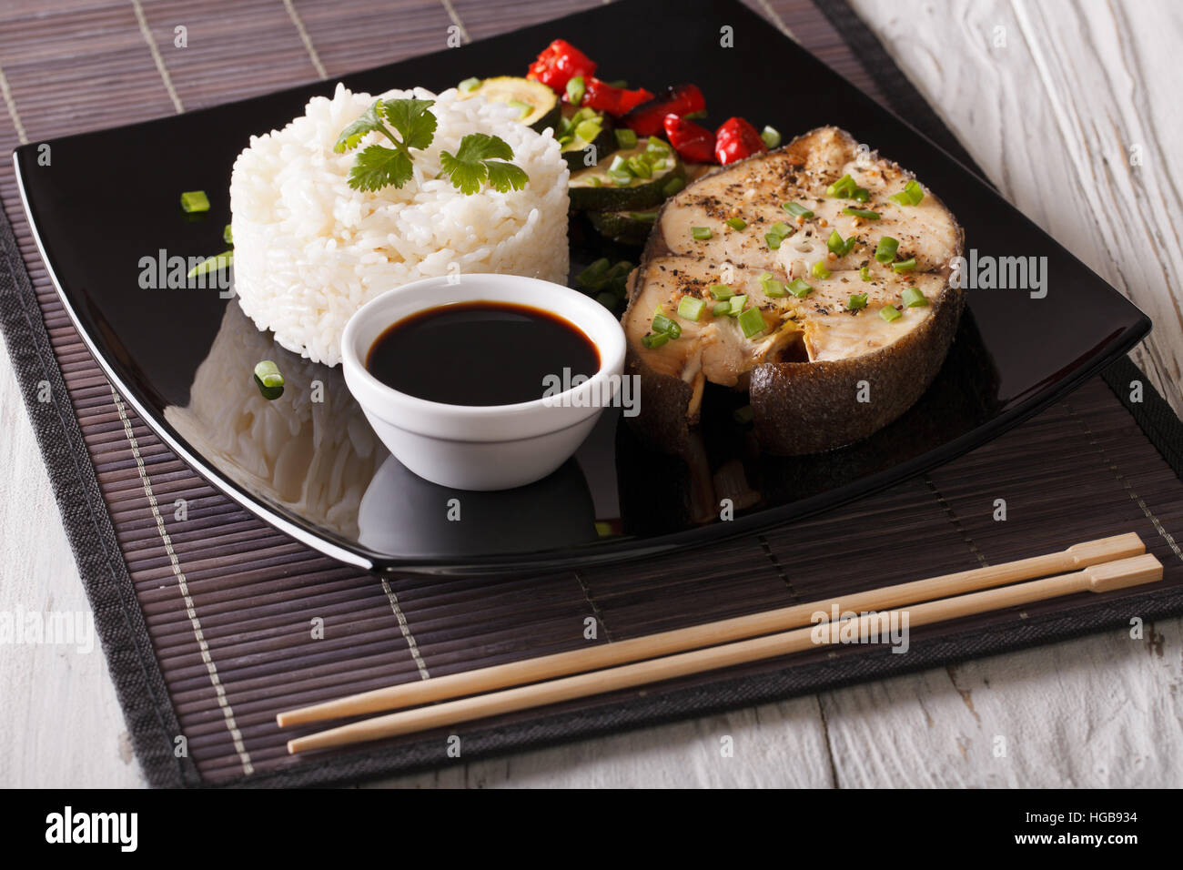 Gebackene Fisch, Reis, Gemüse und Soja-Sauce auf einem Teller. Horizontale Nahaufnahme Stockfoto