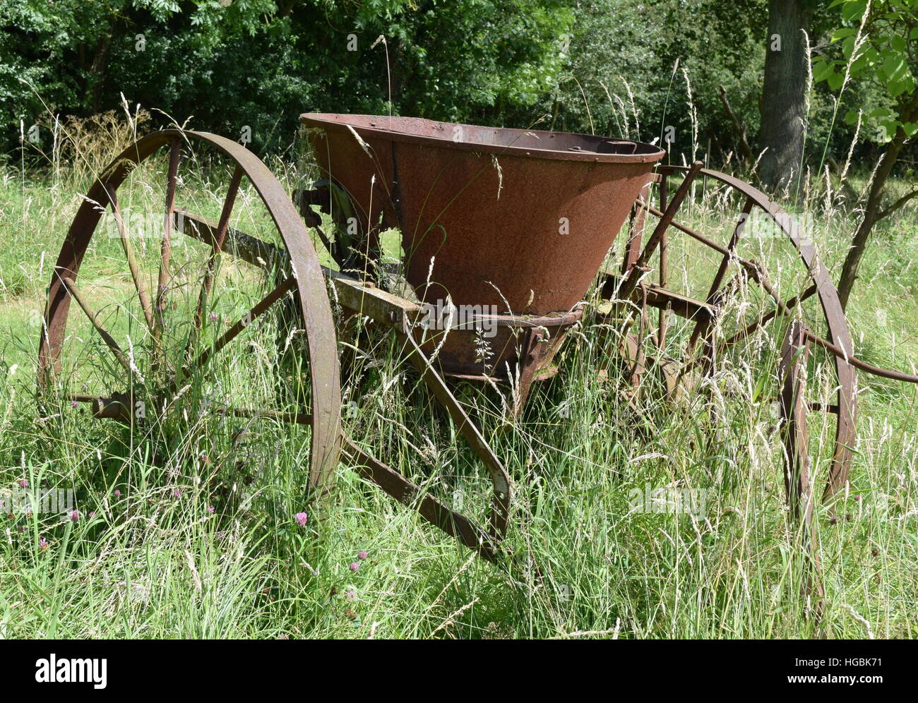 Rostige Oldtimer Landmaschinen lange Gras, Bäume im Hintergrund Stockfoto