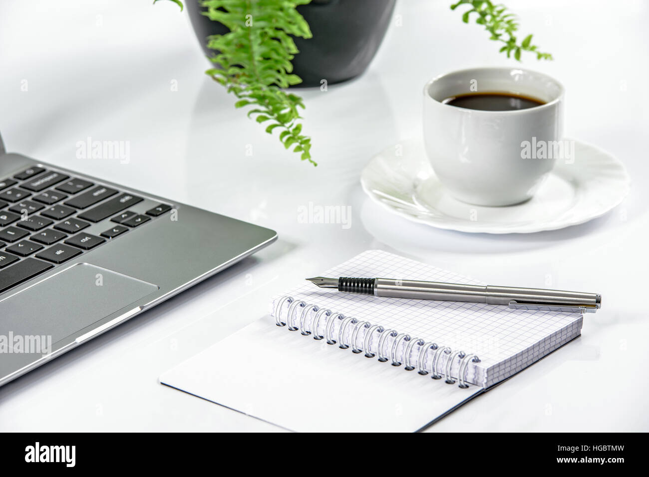 Schlankes Metall Laptop und Stift mit Notizblock auf einen weißen Schreibtisch und Kaffee im Hintergrund Stockfoto