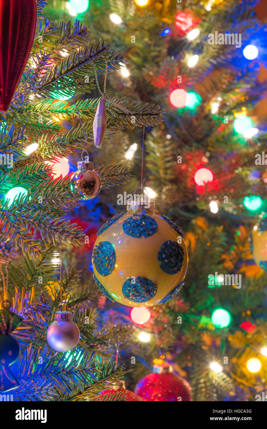 Christbaumschmuck.  Gelbe, glänzende Oberfläche Kugel mit blauen Kreisen, glüht, umgeben von hellen, lebhaften bunten Lichtern Stockfoto