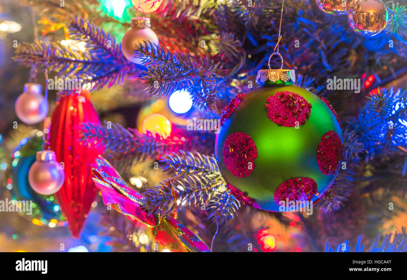 Christbaumschmuck.  Grün, Matte Oberfläche, Kugel mit Magenta Kreisen, glüht, umgeben von bunten Lichtern Mini. Stockfoto