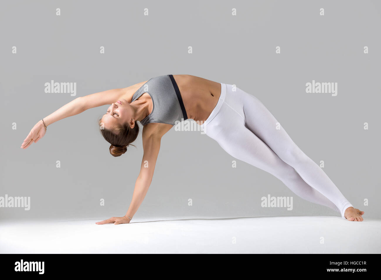 Junge Frau in Vasisthasana Pose, grau Studio-Hintergrund Stockfoto