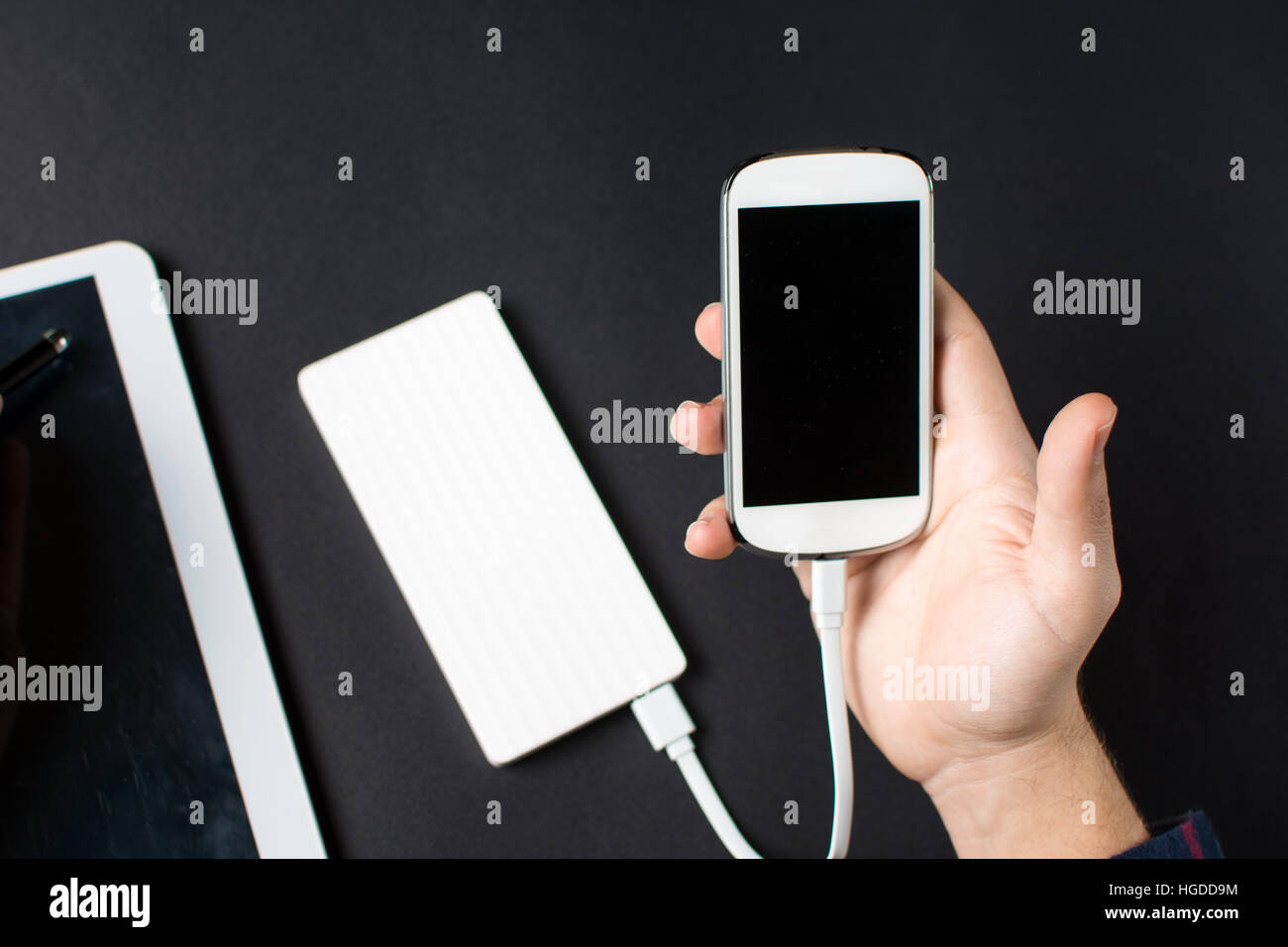 männliche Hände halten ein weißes Handy verbunden, eine Powerbank auf schwarz Stockfoto