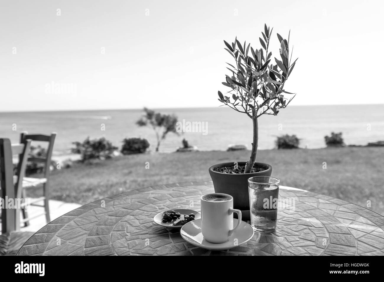 Schwarz und weiß traditionelle Tasse Kaffee auf einem Tisch mit Olivenbaum, Glas Wasser und Marmelade, mit Blick aufs Meer und Himmel in Protaras, Zypern-Insel. Stockfoto