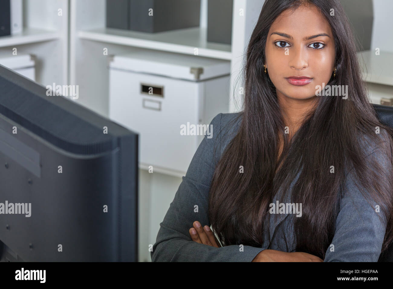Porträt einer schönen leistungsstarke junge indische Asiatin oder Geschäftsfrau im Büro sitzen an einem Schreibtisch Arme gefaltet mit einem computer Stockfoto