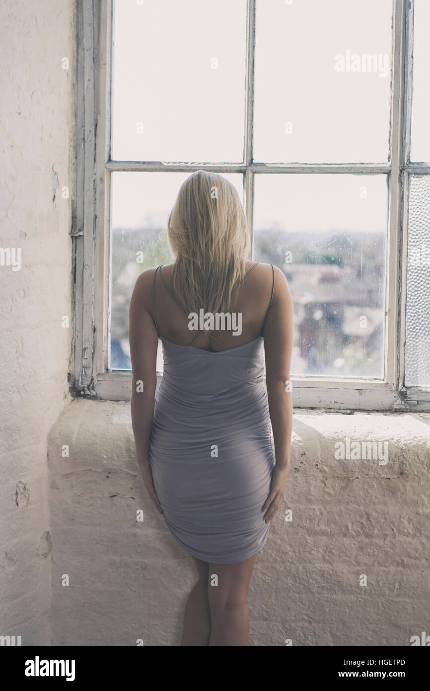 Rückansicht einer blonden Frau am Fenster stehend Stockfoto