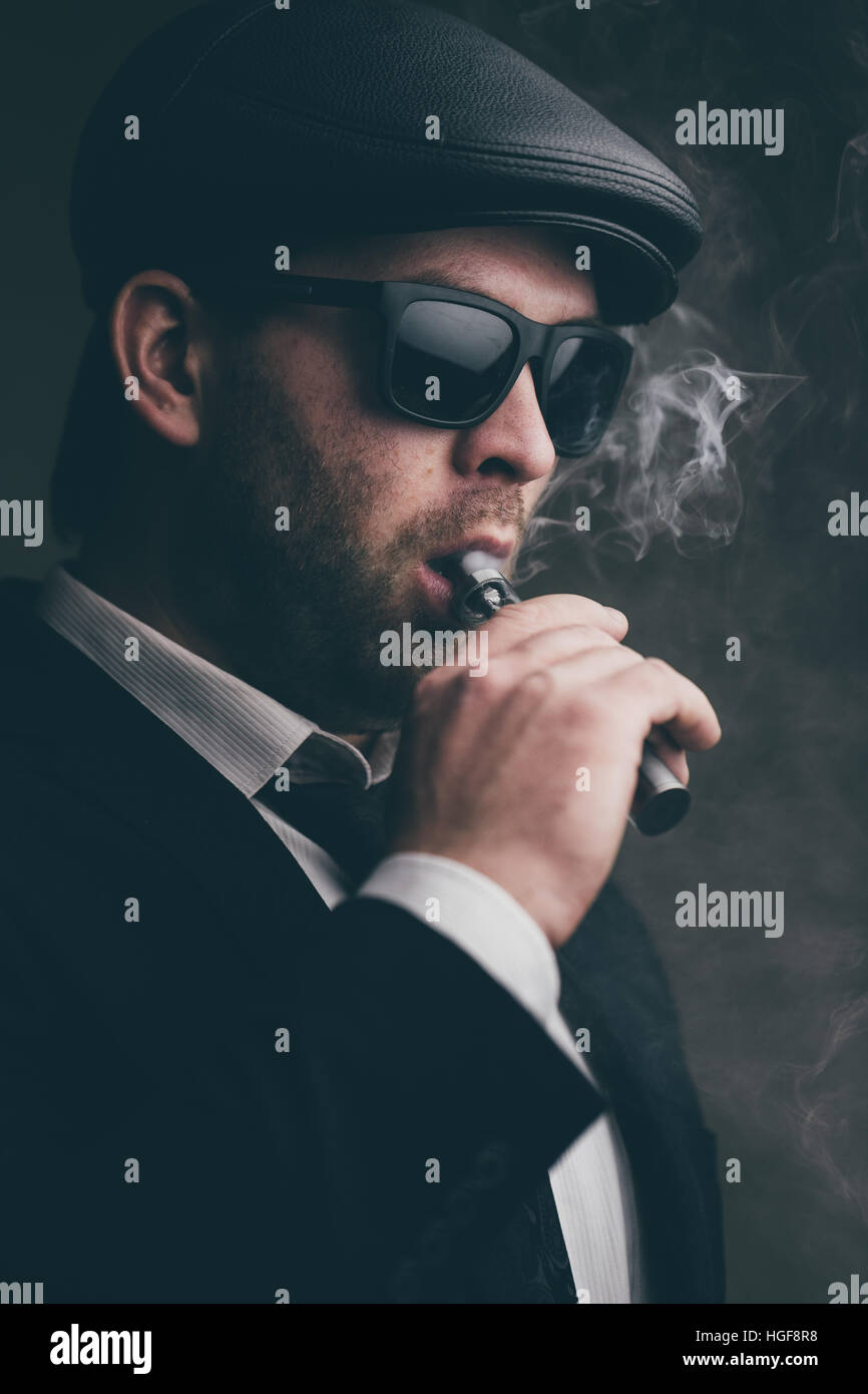 Modische Mann mit Sonnenbrille und eine Lederkappe raucht Stockfoto