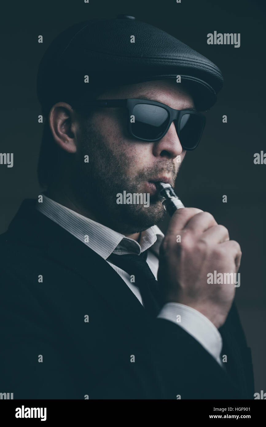 Modische Mann mit Sonnenbrille und eine Lederkappe raucht Stockfoto