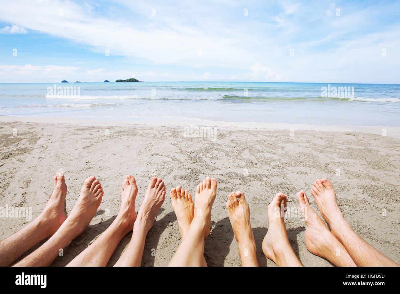 Füße von Familie oder Freunden am Strand, viele Menschen sitzen zusammen auf Sand am Meer, im Sommer Stockfoto