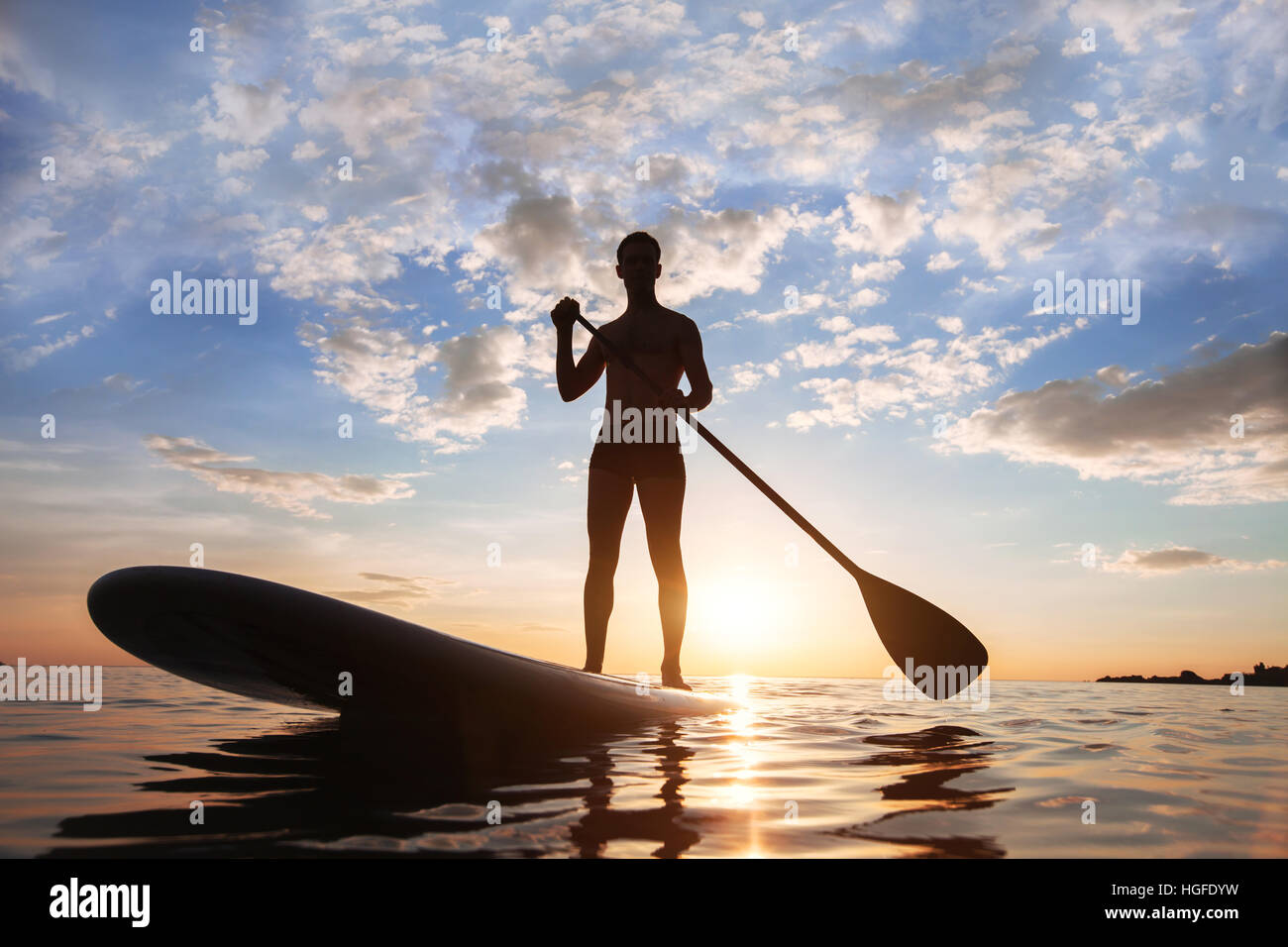 Paddeln Sie, stehend, Silhouette der Mann am Strand bei Sonnenuntergang Stockfoto
