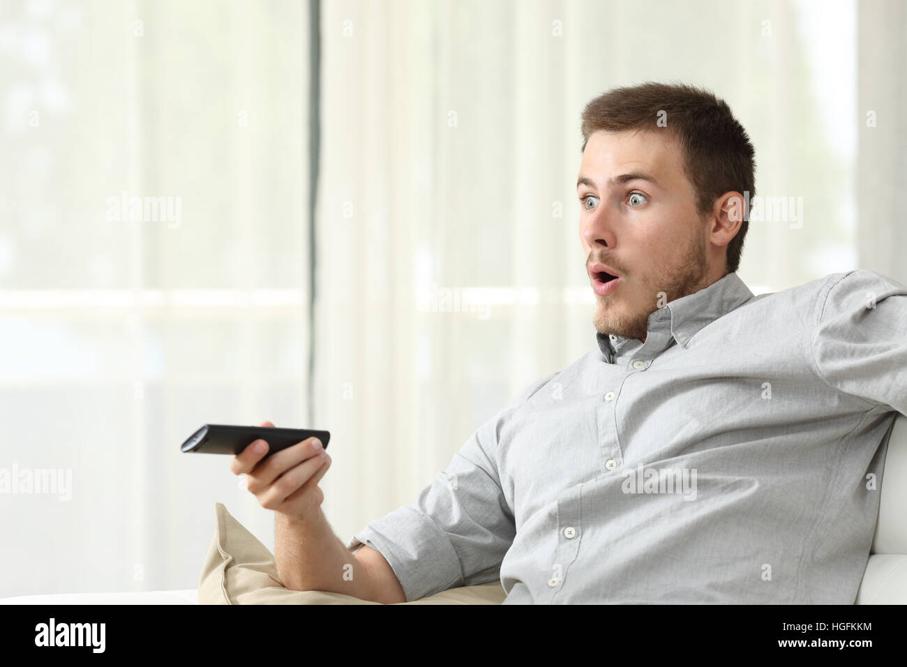 Überrascht Man Zappen vor dem Fernseher sitzen auf einer Couch im Wohnzimmer zu Hause Stockfoto