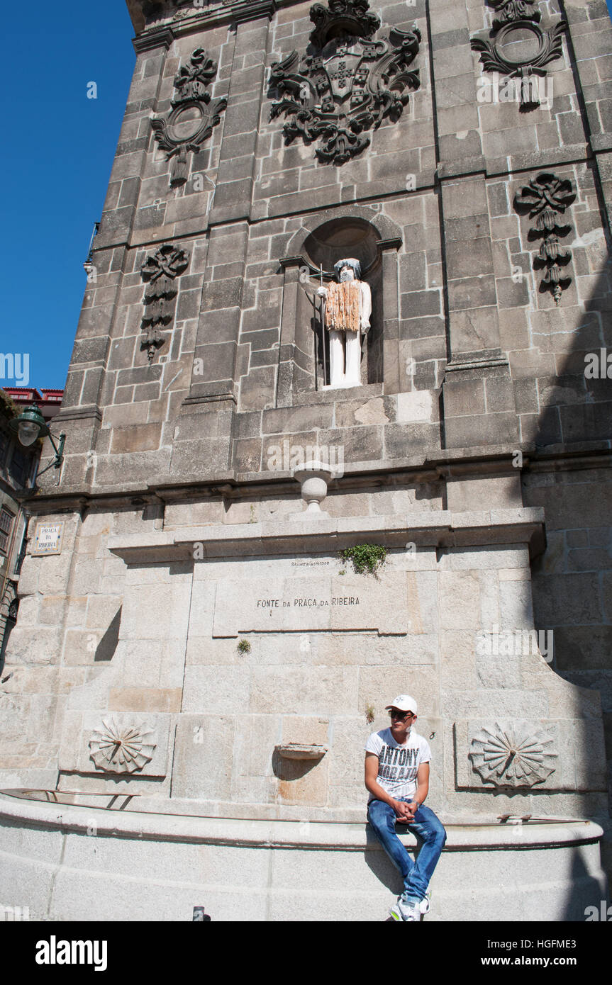 Porto, Portugal, Europa: Ein portugiesischer Mann sitzend auf Fonte da Praca da Ribeira, der Brunnen mit Blick auf den Praça da Ribeira (Fluss) Stockfoto