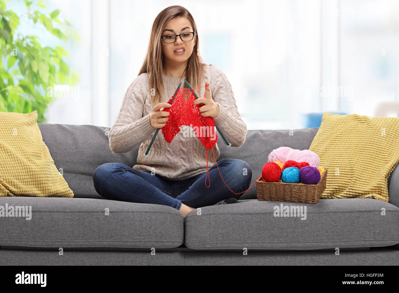 Verwirrt junge Frau auf einem Sofa sitzen und stricken Stockfoto