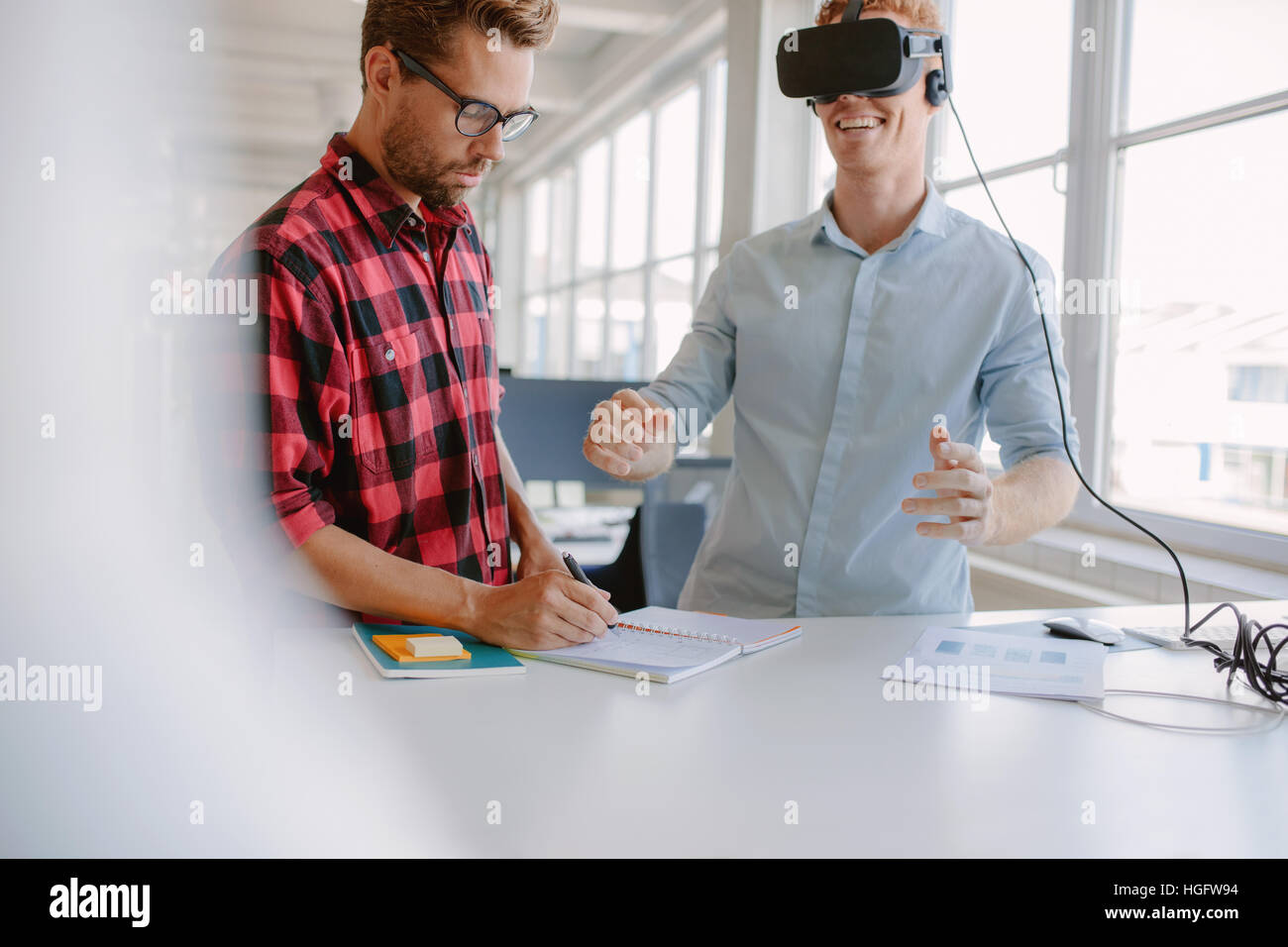 Junger Mann schreiben von Notizen mit Kollegen virtual-Reality-Brille im Büro tragen. Entwickler, die auf augmented-Reality-Technologie arbeiten. Stockfoto