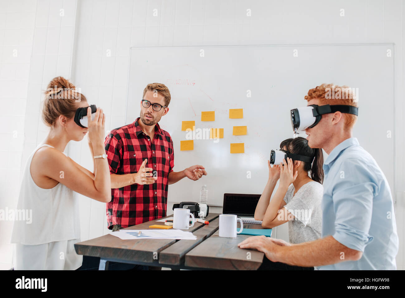 Junge Männer und Frauen sitzen an einem Tisch mit einer virtual-Reality-Brille. Business-Teams testen virtual-Reality-Kopfhörer im Büro treffen. Stockfoto