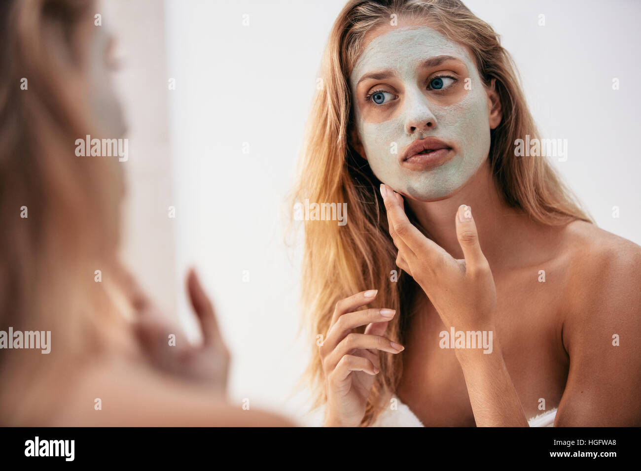 Frau in den Spiegel mit Maske auf ihr Gesicht. Weiblich, kosmetische Gesichtsmaske in Bad anwenden. Stockfoto