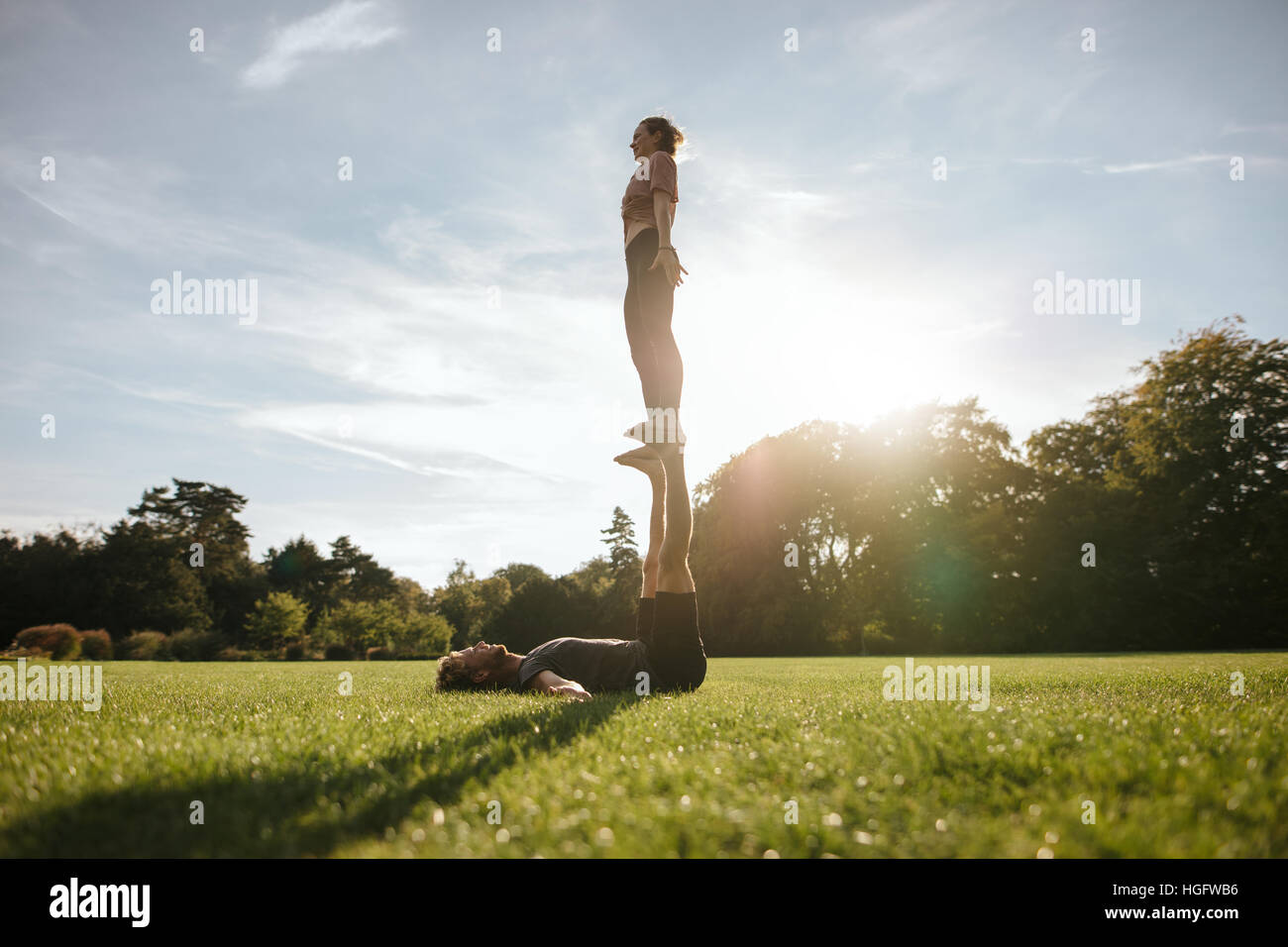 Fit paar tun akrobatische Yoga üben im Park. Mann auf dem Rasen liegen und balancing Frau auf seinen Füßen. Stockfoto