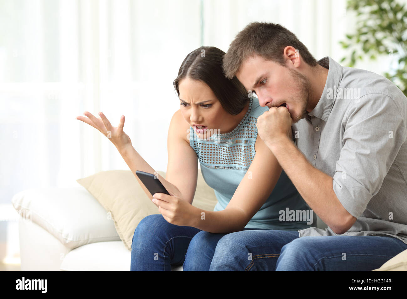 Wütend paar mit Handy sitzen auf einer Couch im Wohnzimmer zu Hause Stockfoto