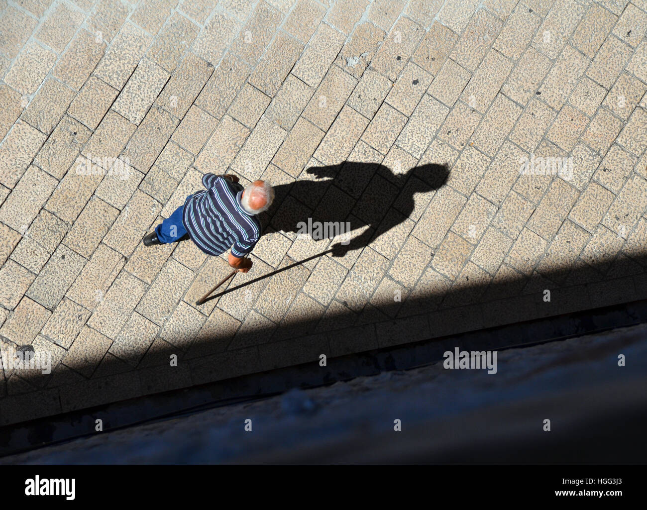 Blick hinunter auf einen alten kroatischen Mann zu Fuß mit einem Stock und sein Schatten in den alten Straßen von Dubrovnik. Stockfoto