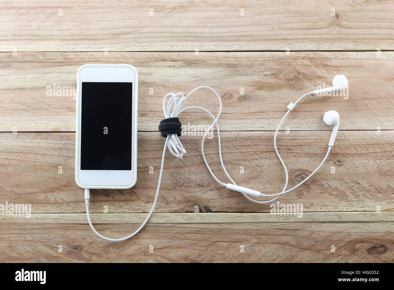 Weißen Smartphone auf braunem Holz Hintergrund und einem Kopfhörer ist Gerät angeschlossen, Konzept von Musik und Technologie. Stockfoto