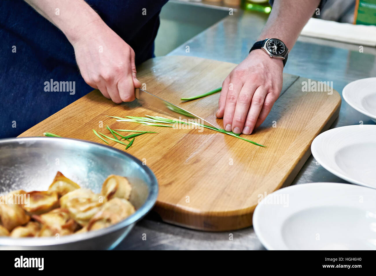 Koch schneidet Frühlingszwiebeln für Schüsseln von Knödel Stockfoto