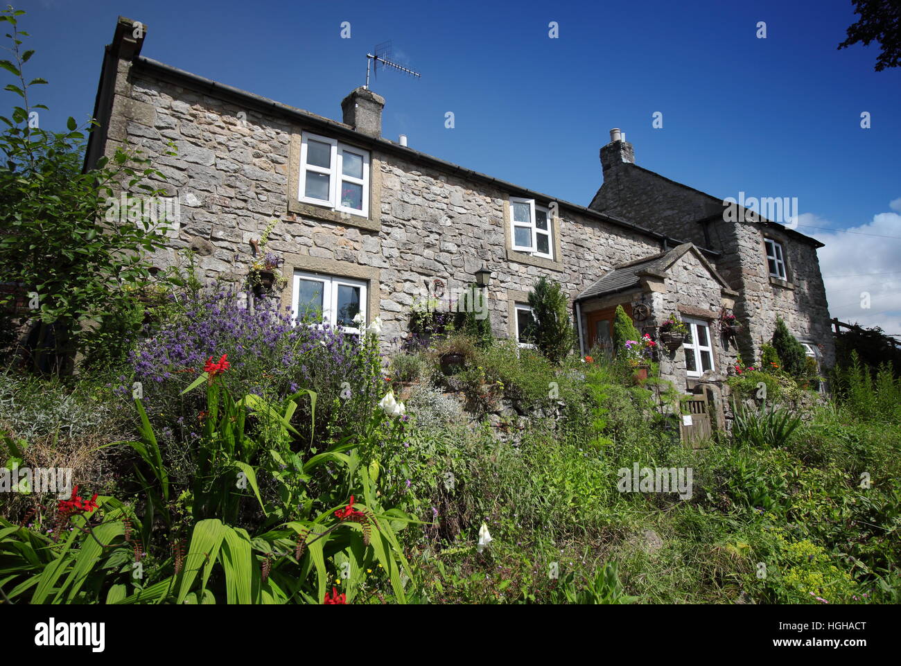 Cottage-Garten als Frontmann einer traditionellen Stein-Eigenschaft in einem hübschen Dorf in der englischen Landschaft an einem warmen Sommertag Stockfoto