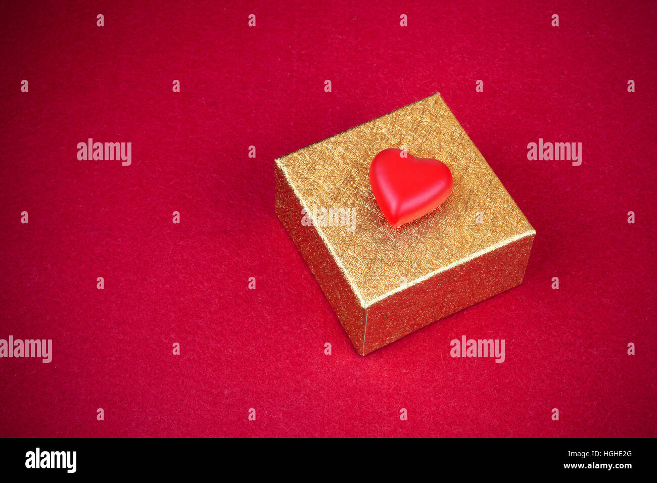 Rotes Herz auf einem leuchtenden goldenen gelben Kasten im roten Hintergrund. Stockfoto