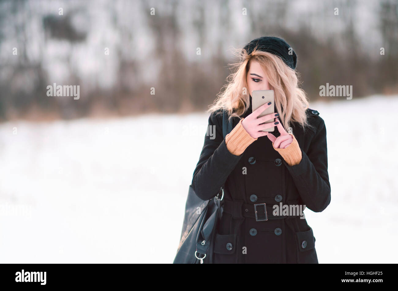 Junge alternative Blondine in schwarzer Kleidung Blick auf Telefon Stockfoto