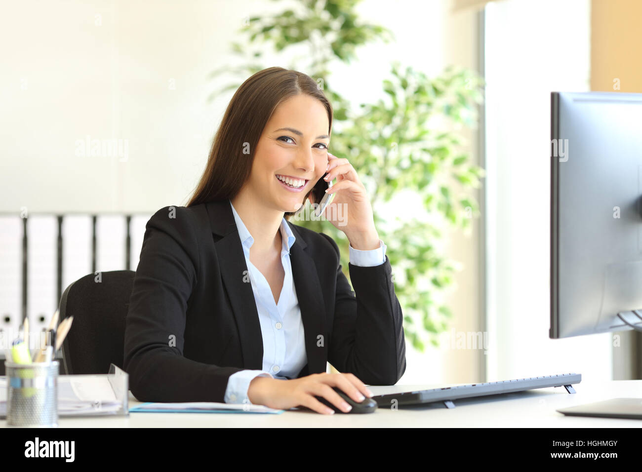 Porträt eines glücklichen Exekutive Anzug Sie den Kundendienst am Telefon anrufen und Blick in die Kamera sitzt auf dem Schreibtisch im Büro Stockfoto