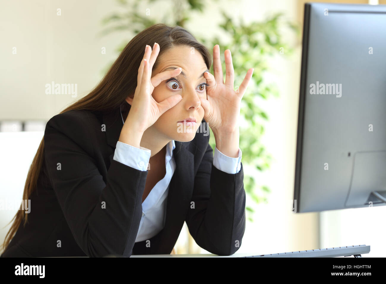 Verschlafene Geschäftsfrau wach halten Sie die Augen öffnete mit den Fingern beobachten einen Desktop-Computer-Monitor im Büro zu bleiben Stockfoto