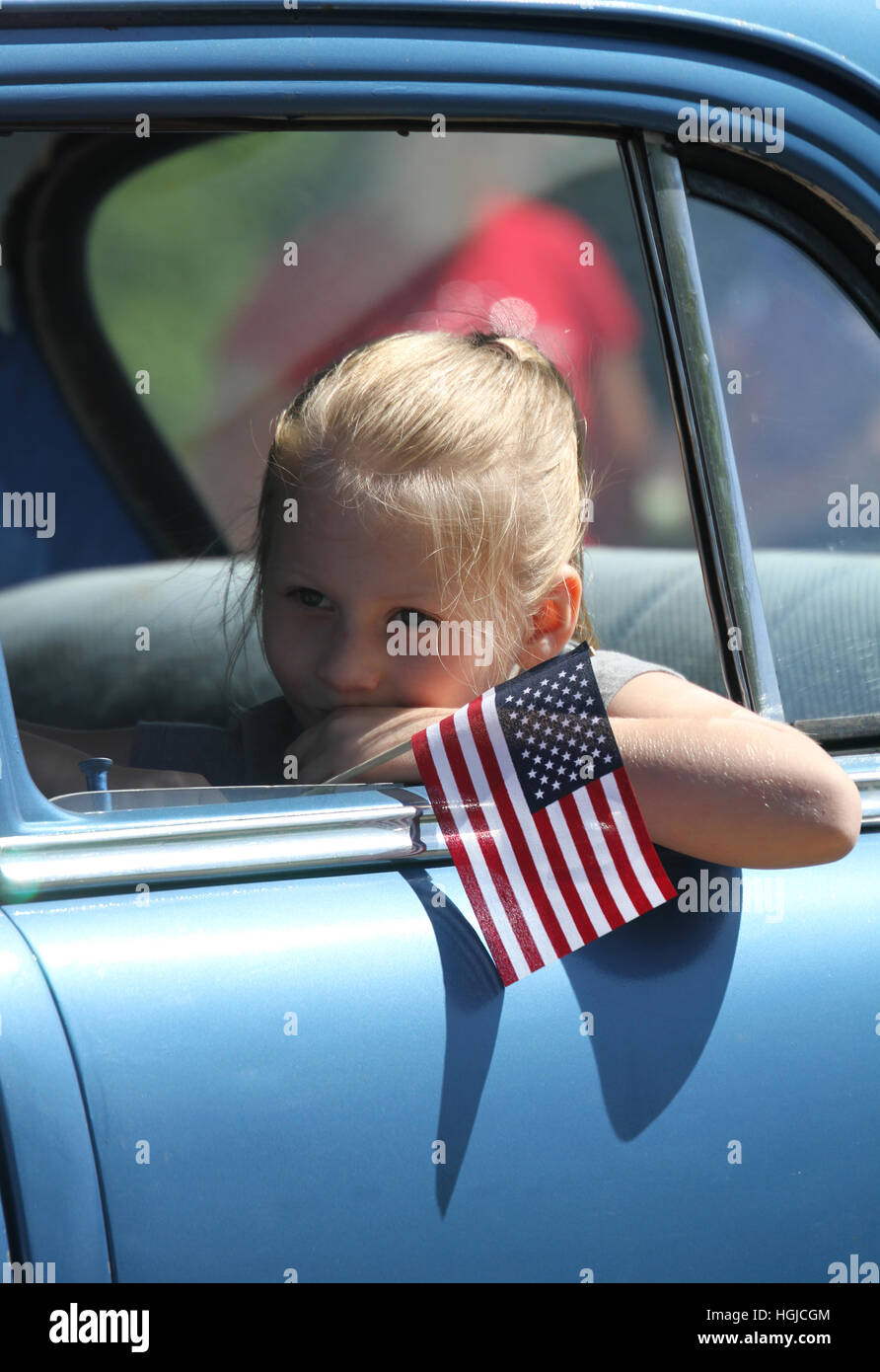 Ein junges Mädchen träumt wehmütig während der Fahrt in einem Auto hält ein kleines uns Flagge. Stockfoto