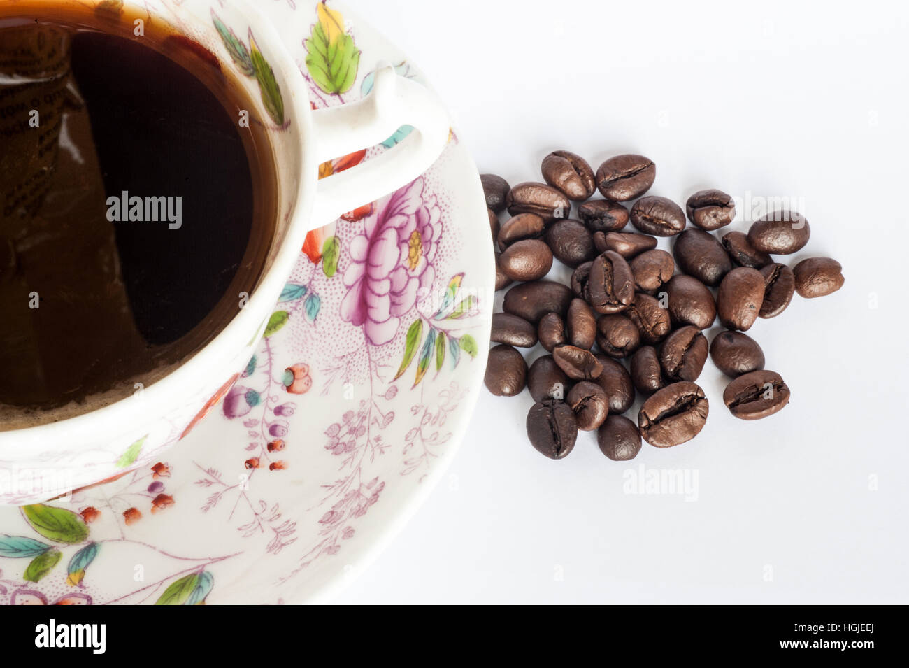 Eine viktorianische Tasse und Untertasse mit Kaffee mit ganzen Kaffeebohnen auf weißem Hintergrund mit textfreiraum gefüllt. Stockfoto