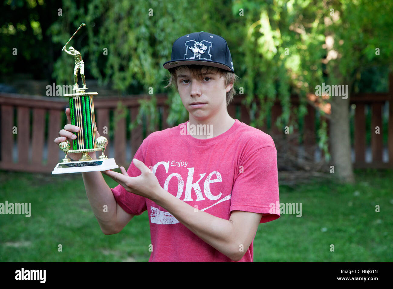 Teen Junge hält stolz seinen ersten Platz Golf Trophy in seinem umzäunten Garten zu Hause. St Paul Minnesota MN USA Stockfoto