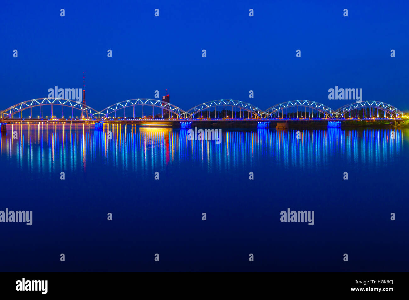 Beleuchtete Eisenbahnbrücke und Reflexion im Fluss Daugava in der Dämmerung. Riga, Lettland Stockfoto