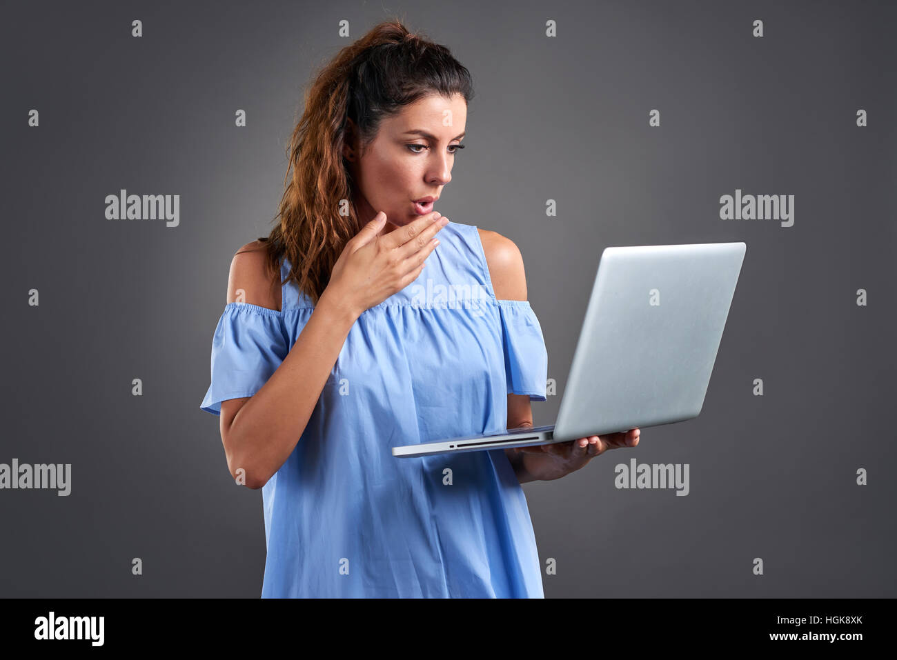 Eine schöne junge Frau stehend und Feelling überrascht beim Betrachten eines Laptops in der Hand. Stockfoto