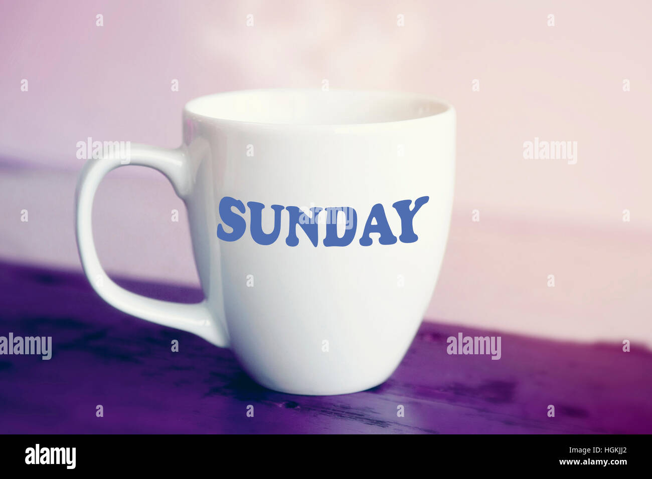 weiße Tasse mit dem Wort Sonntag drauf auf lila Holztisch Stockfoto
