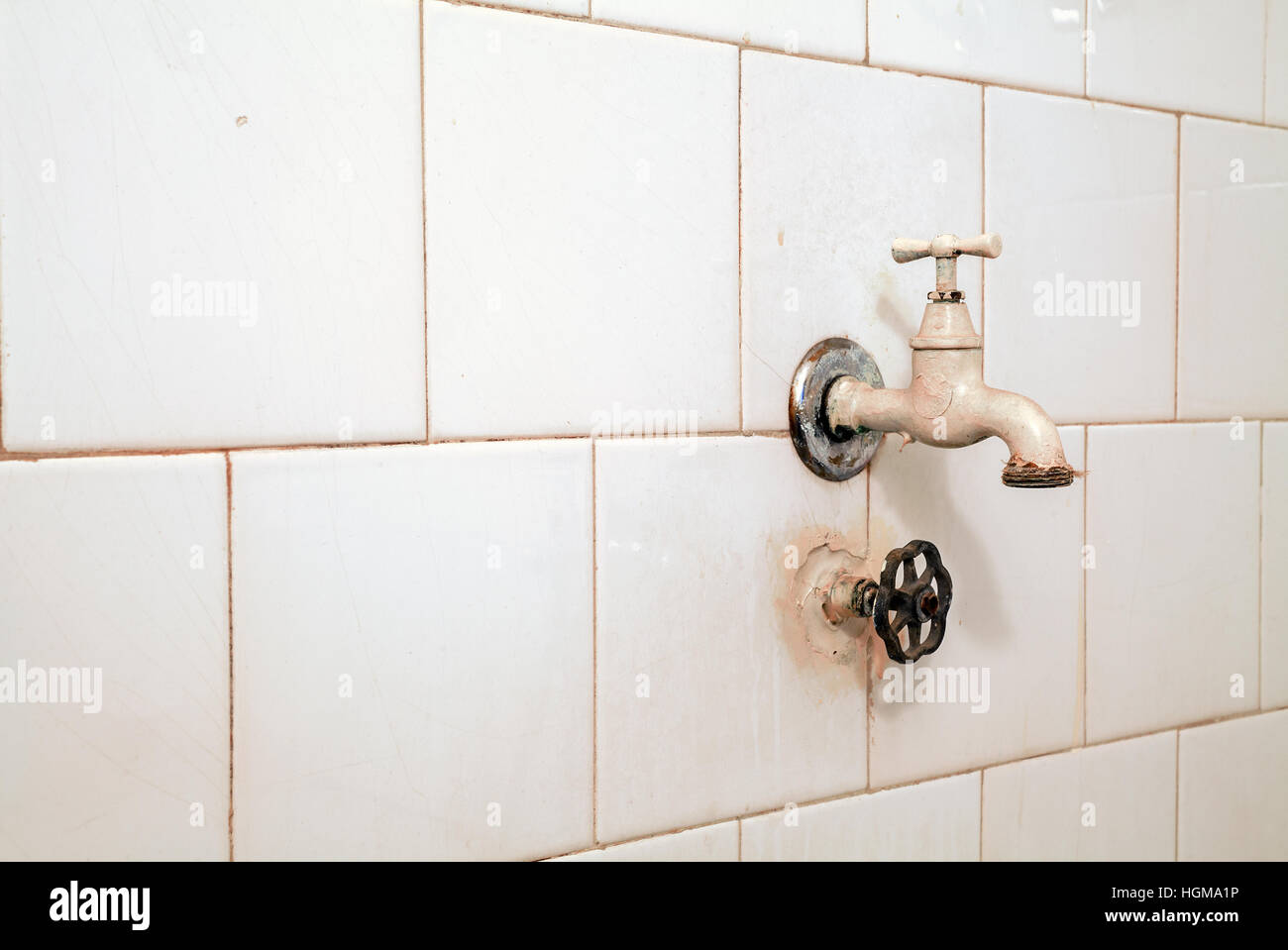 Einzelheiten über eine alte, trockene und unbenutzte Wasserhahn auf weißen Badezimmerfliesen. Stockfoto