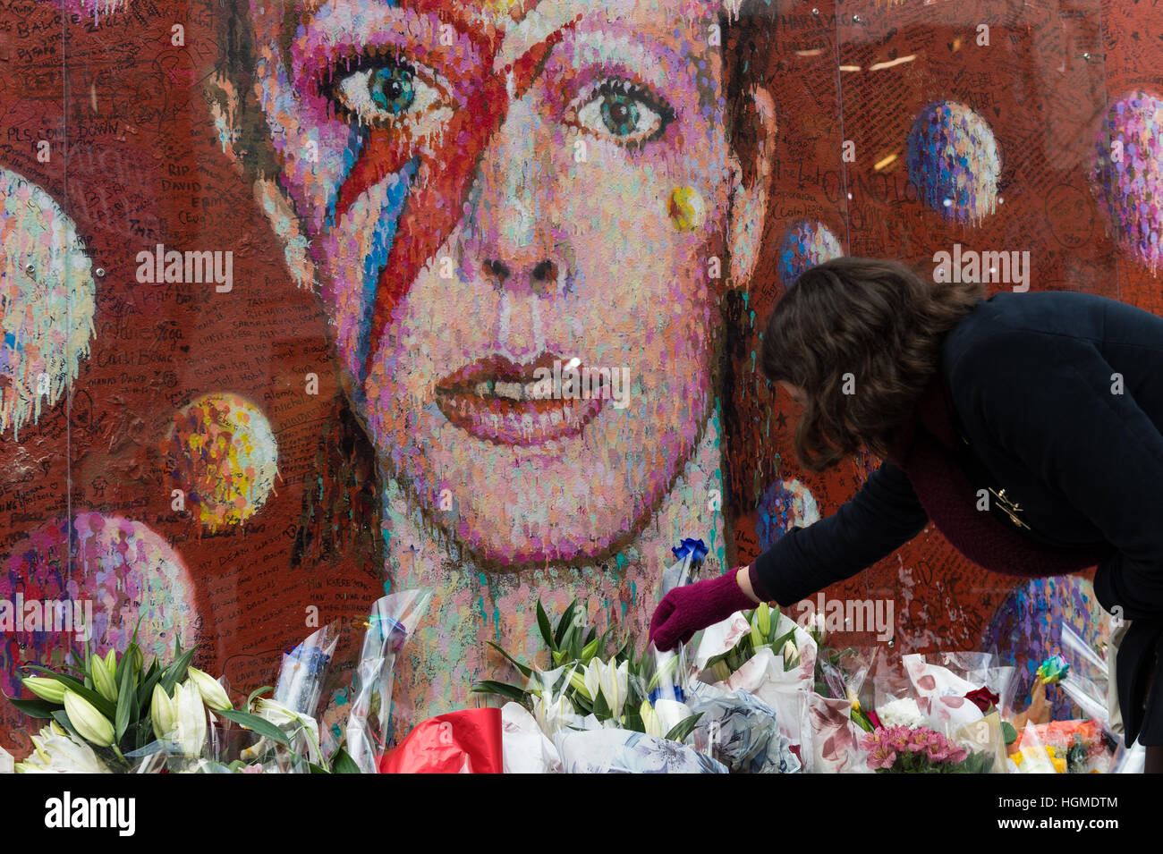 London, UK. 10. Januar 2017. Fans sammeln durch das Wandbild von David Bowie im Geburtshaus des Künstlers Brixton zum Gedenken an den ersten Todestag des Musikers. Brixton Wandbild, Bowies Gesicht von Aladdin Sane Albumcover zeigt, wurde der große Gedenkstätte nach der Star-Tod am 10. Januar 2016. Wiktor Szymanowicz/Alamy Live-Nachrichten Stockfoto