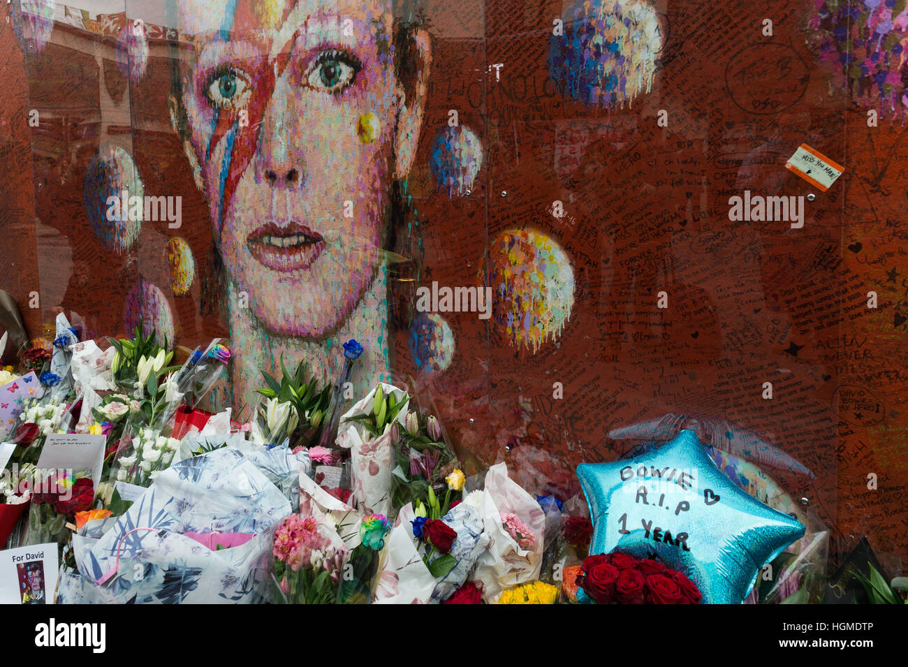 London, UK. 10. Januar 2017. Fans sammeln durch das Wandbild von David Bowie im Geburtshaus des Künstlers Brixton zum Gedenken an den ersten Todestag des Musikers. Brixton Wandbild, Bowies Gesicht von Aladdin Sane Albumcover zeigt, wurde der große Gedenkstätte nach der Star-Tod am 10. Januar 2016. Wiktor Szymanowicz/Alamy Live-Nachrichten Stockfoto