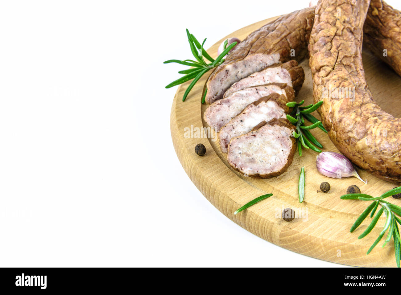 Geschnittene Wurst auf einem Holzbrett und Rosmarin, Pfeffer und Knoblauch auf weißem Hintergrund Stockfoto
