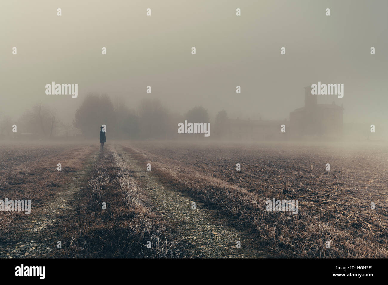 Frau in der Ferne Blick auf eine Kirche im dichten Nebel von der Region Lombardei in Italien während der Winter, gefrorenen Mais-Feld Stockfoto