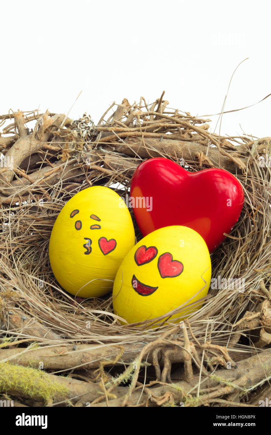 Zwei Ostereier bemalt mit Emojis, eins in der Liebe und anderen küssen, in isolierten weißen Hintergrund in ein Nest gelegt. Stockfoto