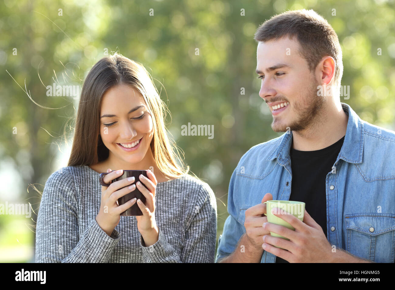 Vorderansicht eines Paares flirten und reden in einem Park mit einem grünen Hintergrund bei Sonnenuntergang Stockfoto