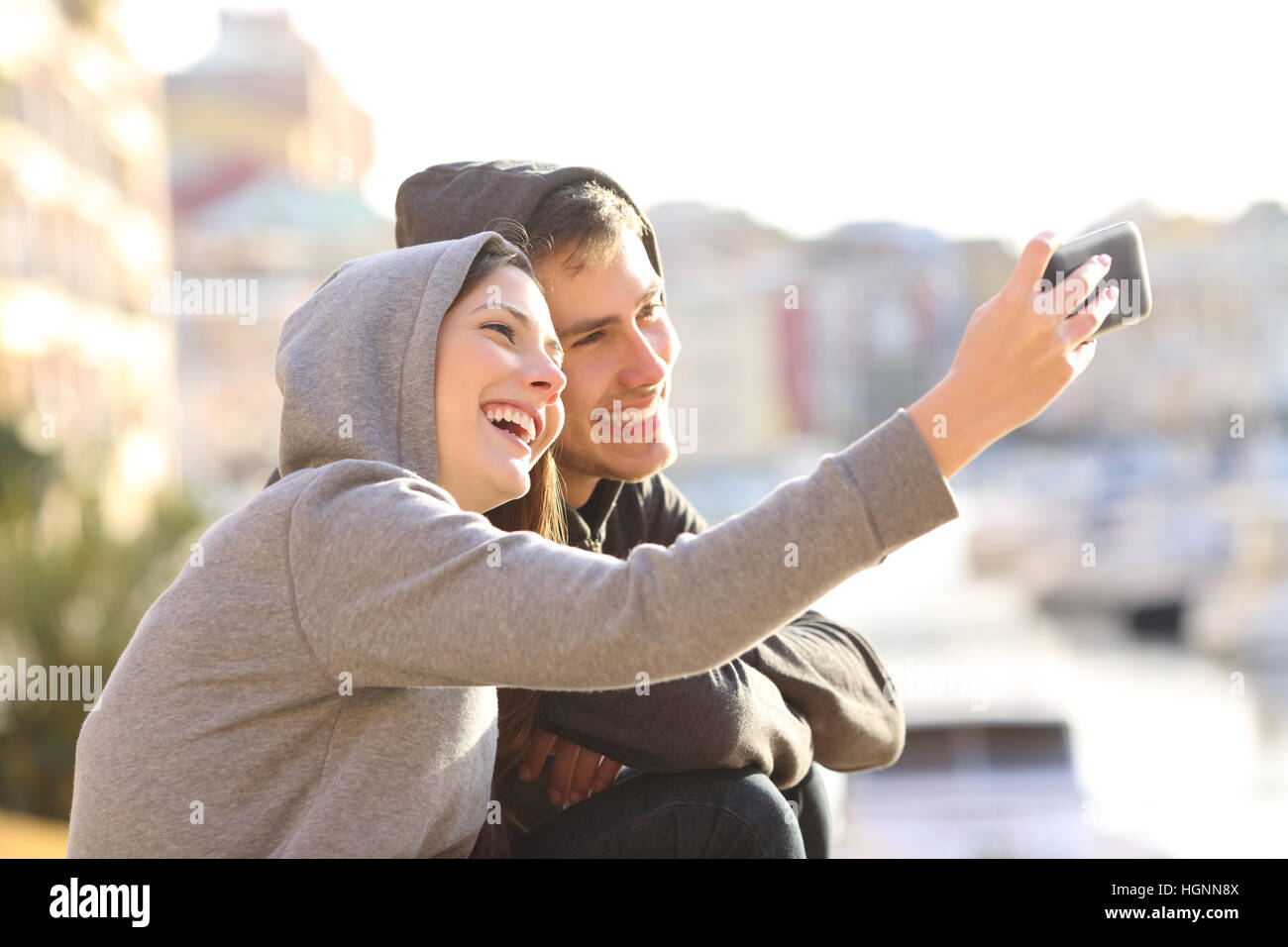 Paar Teenager nehmen ein Selbstporträt mit einem Smartphone im Freien an Feiertagen mit einem Hafen im Hintergrund Stockfoto