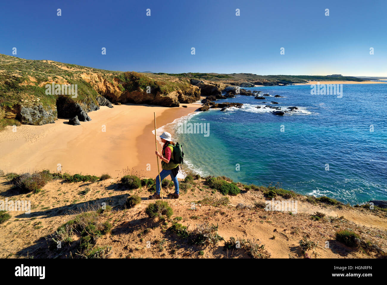 Frau mit Rucksack und Wanderstock trekking entlang einer sandigen Küstenpfad entlang einsamer Strände und eine ruhige blaue Meer Stockfoto